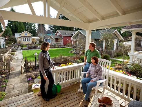 Brian and Colleen Ducey, right, chat with neighbor Eileen McMackin on their front porch in Shoreline, Wash., where eight bungalows share a yard, garden and commons building.